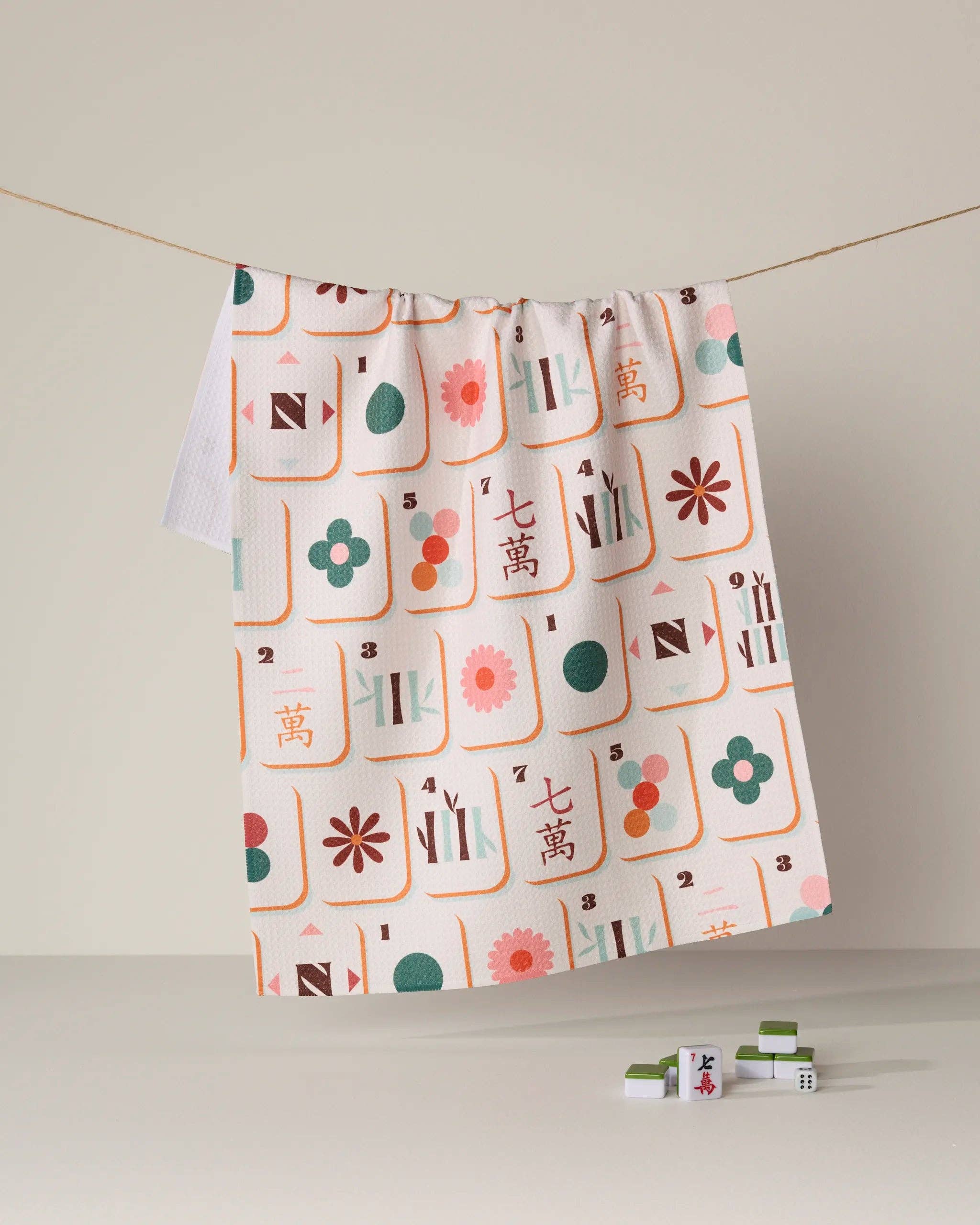 Mahjong tile print tea towel in pink green orange on cream background hanging on cord