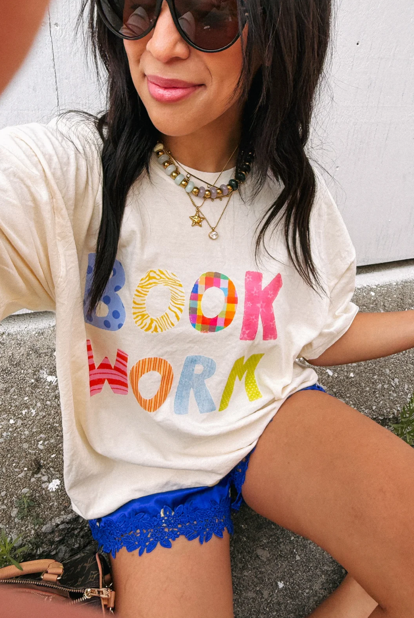 Ivory graphic tee with multicolor BOOK WORM letters in patterned bold font