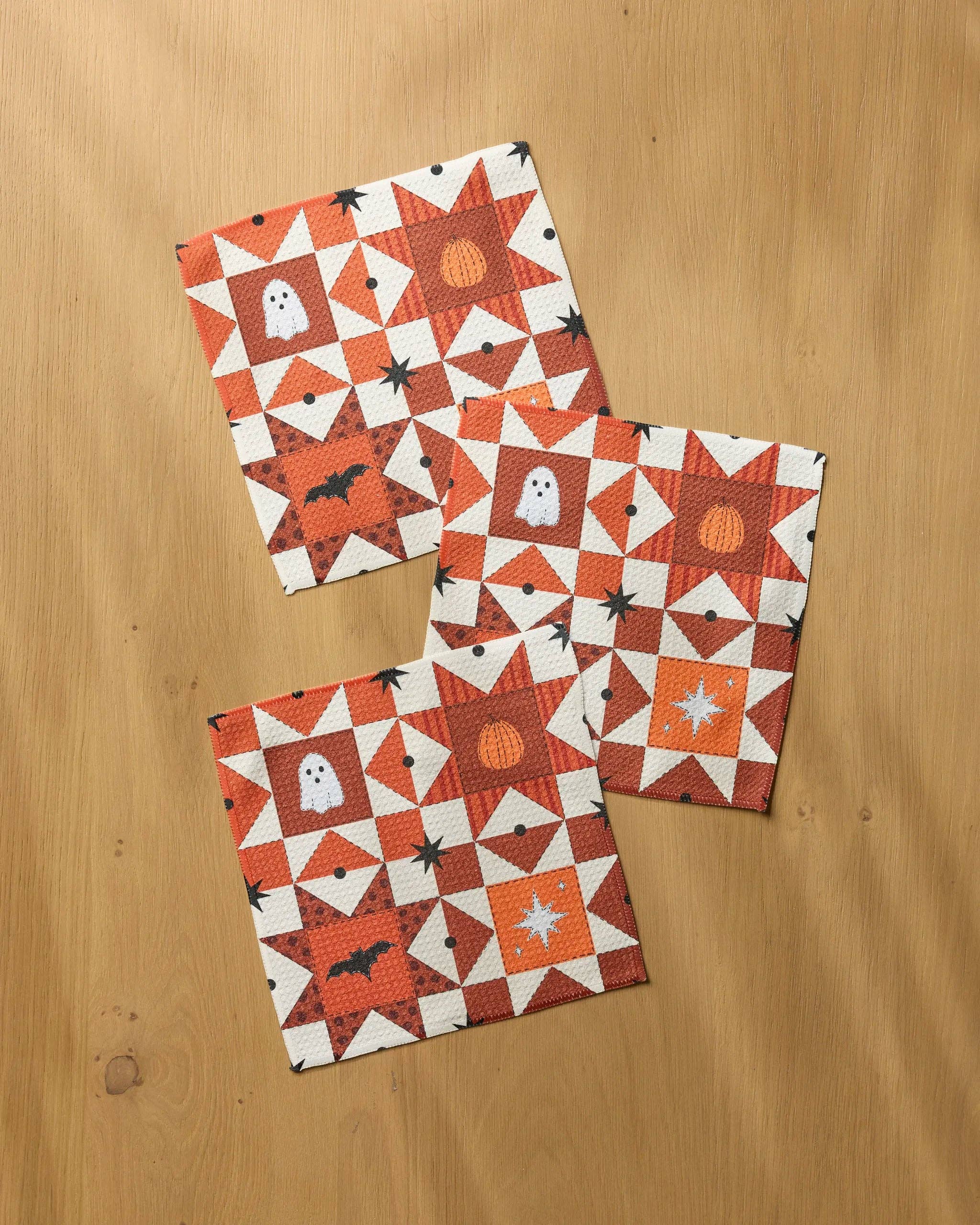 Three Halloween quilted-pattern dishcloths with ghosts, pumpkins, and bats in orange and white