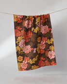 Floral tea towel with pink, orange, and gold flowers on dark brown background hung on rope