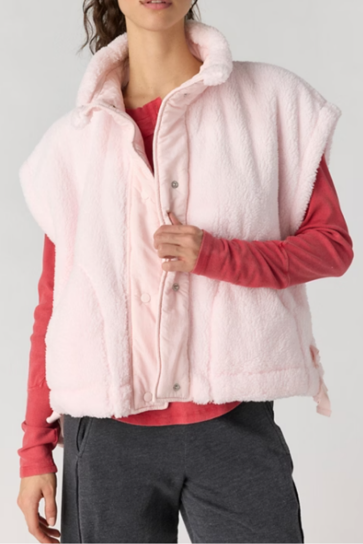 Light pink fleece vest with snap-front placket and funnel neck over red long-sleeve top