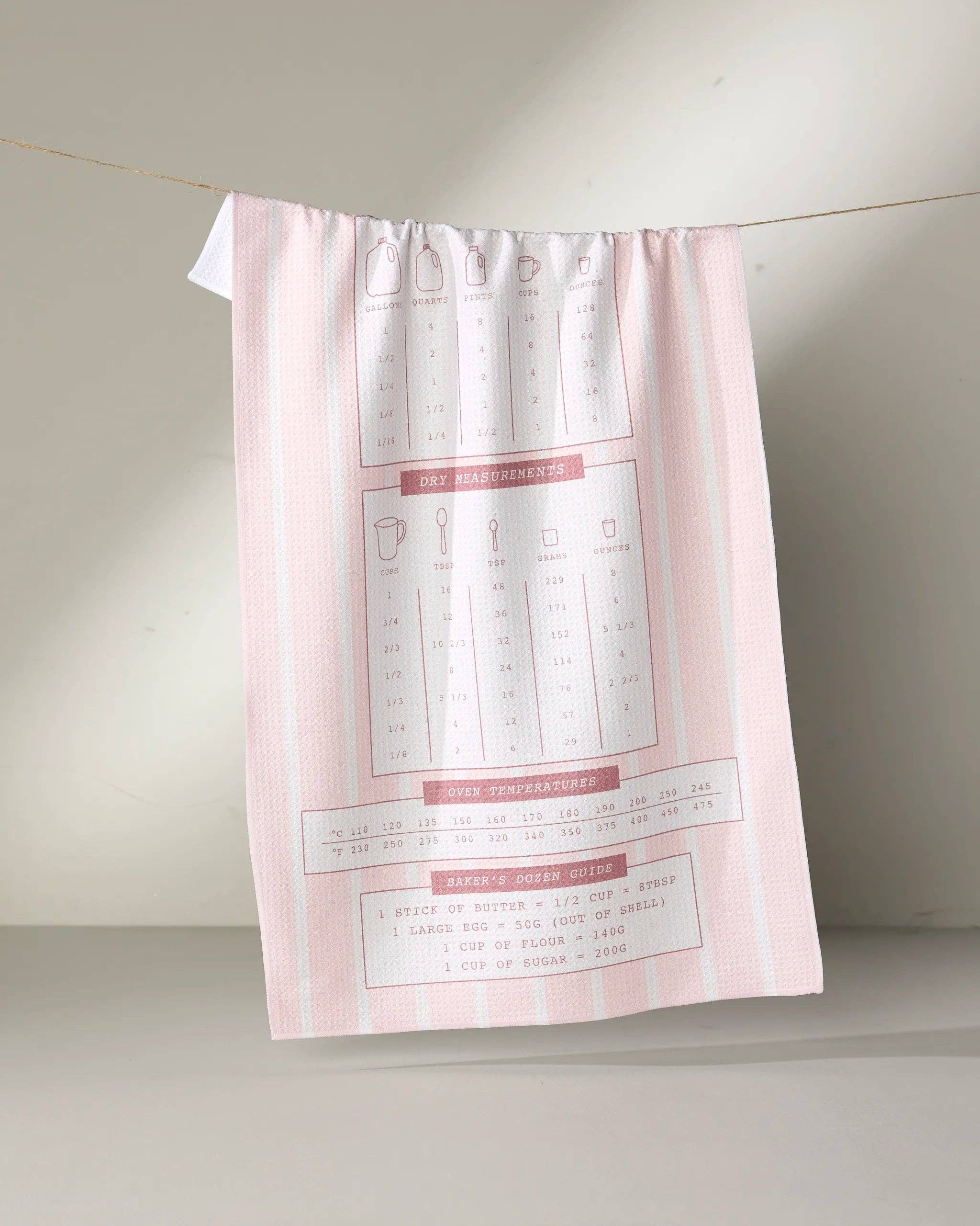 Pink striped tea towel with baking measurement charts hanging on a rope