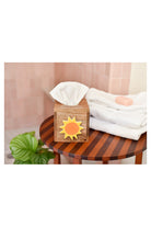 Wooden tissue box with colorful sun emblem on striped table beside folded towels