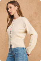 Cream knit cardigan with multicolor velvet buttons, ribbed hem and cuffs, paired with blue jeans