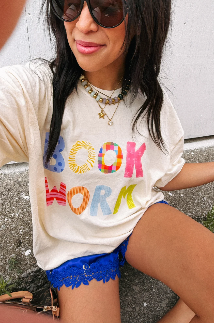 Ivory graphic tee with multicolor BOOK WORM letters in patterned bold font