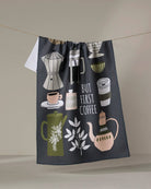 Dark gray coffee-themed tea towel with illustrated brewing tools and 'But First Coffee' text